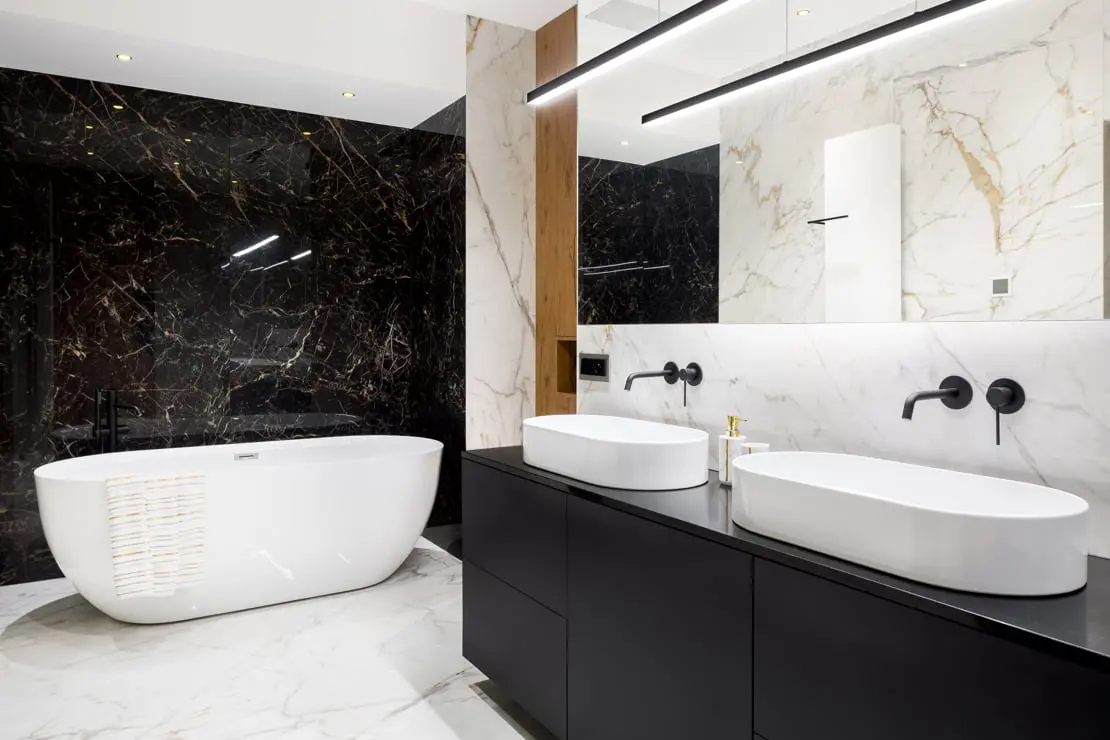 Luxe badkamer met dubbele wastafel, ingebouwde zwarte kranen en een bad aan het einde van de kamer