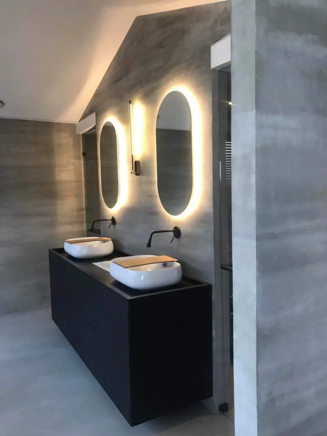 Mikrocement na tleh in stenah minimalistične kopalnice, okrašene s črnimi pipami